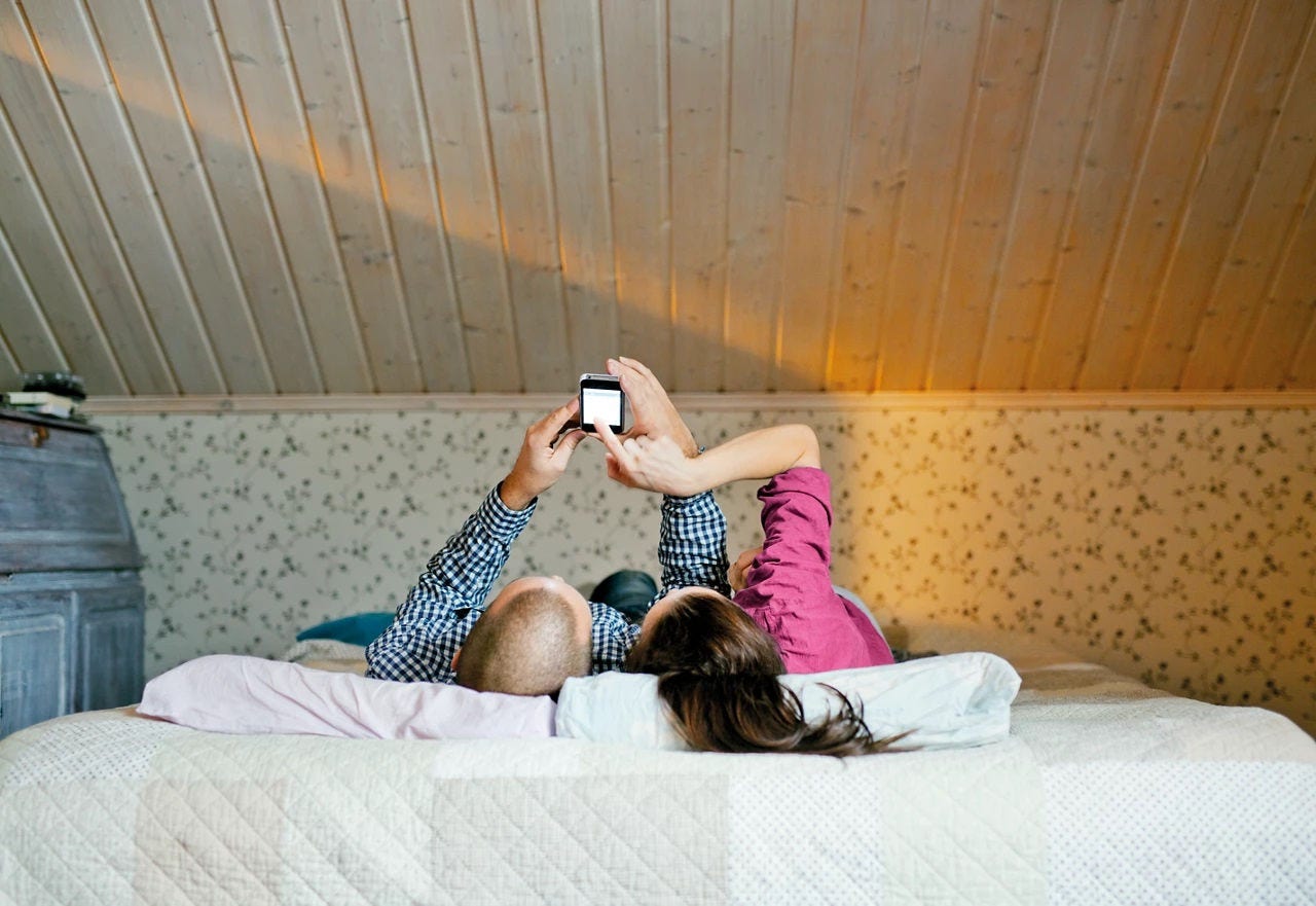 a couple laying down on the bed looking at a cell phone